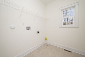 Empty laundry room with white walls, a wire shelf, a window, and plumbing hookups for a washer and dryer.
