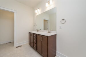A modern bathroom features a double sink vanity with a large mirror, wooden cabinets, and two wall-mounted lights above.