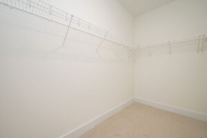 Empty walk-in closet with beige carpet, white walls, and white wire shelving along two walls.