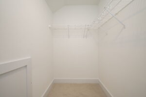 Empty walk-in closet with white walls, beige carpet, and white wire shelving.