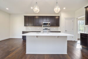 Modern kitchen with dark wood cabinets, stainless steel appliances, white countertops, a white island, and pendant lighting.