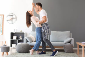 A happy couple dancing together in a bright, cozy living room, with modern furniture and decor around them.