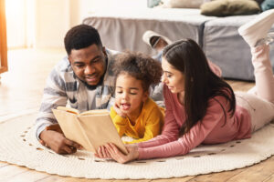 A diverse family lies on a rug reading a book together in a cozy living room.