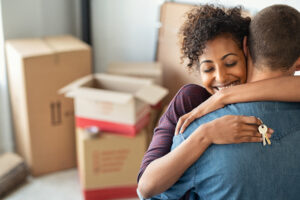 A joyful woman hugging a man and holding keys, with moving boxes in the background, conveying a new home celebration.