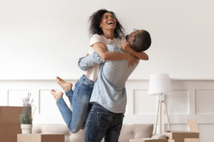 A joyful young woman embracing a man in a living room, with open cardboard boxes indicating a new home.