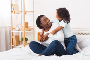 A joyful mother and her young son embracing and laughing together on a bed in a bright, cozy bedroom.