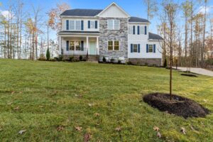 A two-story suburban home with a gray and white facade, surrounded by a freshly mowed lawn and young trees under a clear blue sky.