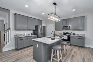 Modern kitchen with gray cabinets, stainless steel appliances, a central island with bar stools, and a stylish chandelier.