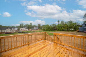 View from a wooden deck overlooking a residential construction site with partially built houses and trees under a blue sky with clouds.