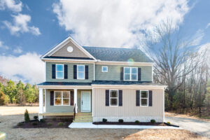 New two-story house with pale blue siding, white trim, and a covered front porch, located in a clearing with trees in the background under a partly cloudy sky.