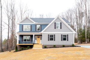 A new two-story house with blue siding, white trim, and a yellow front door, surrounded by a bare yard and leafless trees.