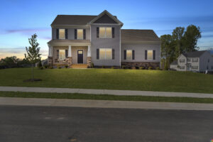 A two-story suburban house with beige siding, a covered front porch, and a well-manicured lawn during dusk.