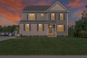 Two-story house with illuminated windows, gray siding, and a green lawn in front, set against a dusk sky with orange and purple hues.