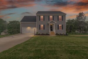 A two-story suburban home with a gray exterior and attached garage under a colorful sunset sky.