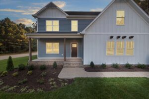 Modern two-story house with blue siding, large windows, and a porch. This new home is surrounded by a grassy lawn and shrubs.