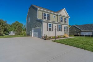 Two-story house with gray siding, white trim, double garage, and well-maintained lawn, set against a bright blue sky.