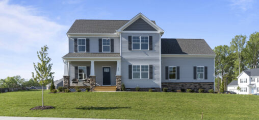 New two-story house with gray siding, white trim, front porch, and a small front yard with a young tree.