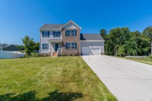 Two-story suburban home with a large driveway and lush green lawn under a clear blue sky.