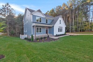 A modern two-story blue house in Virginia with a manicured lawn and wooded backdrop, under a clear blue sky.