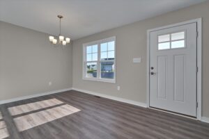 A bright, empty room with large windows, a chandelier, wooden flooring, and a white door with a small window.