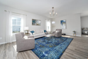 Bright, modern living room with large sofa, two armchairs, a blue patterned rug, wood flooring, and abstract wall art.