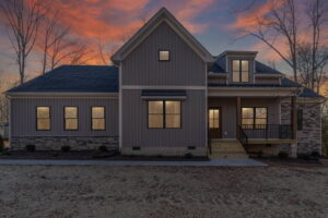 A modern house with gray siding under a vibrant sunset sky, featuring large windows and a front porch.
