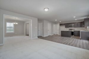 Open-concept living area with carpet, adjacent dining room featuring a chandelier, and a kitchen with dark cabinets, granite countertops, and stainless steel appliances.