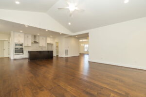 Spacious, empty interior of a modern home featuring hardwood floors, white cabinetry, stainless steel appliances, and vaulted ceilings with a ceiling fan.