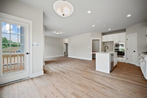 Spacious and modern kitchen and dining area with light wood floors, white cabinets, stainless steel appliances, and ample natural light from windows and doors.