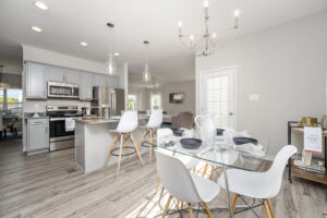 Modern kitchen and dining area with white cabinetry, stainless steel appliances, a dining table set for four, and pendant lighting.