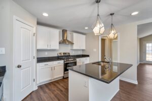 Modern kitchen interior with white cabinetry, stainless steel appliances, a central island, and pendant lighting in a newly constructed home.