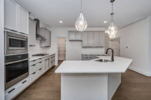 Modern kitchen with white cabinets, stainless steel appliances, and a large central island with a sink. The kitchen features pendant lighting and hardwood flooring.