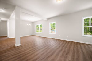 Empty living room with hardwood floors, white walls, and multiple windows providing natural light.