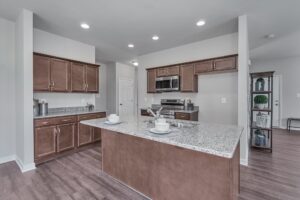 A modern kitchen with brown cabinets, a granite island with place settings, stainless steel appliances, and recessed lighting.