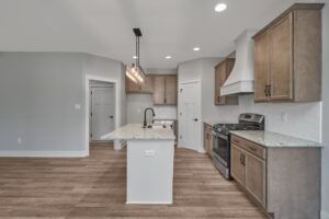 Modern kitchen with hardwood floors, wooden cabinets, granite countertops, stainless steel appliances, central island with sink, and pendant lighting.