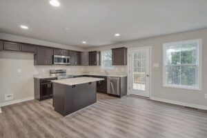 Modern kitchen with dark wood cabinets, stainless steel appliances, and a granite countertop island. The room has hardwood floors, recessed lighting, and a door leading to an outdoor area.