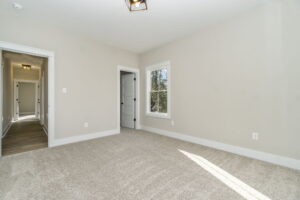 Empty room with beige walls, two windows, and gray carpet, featuring an open door leading to a hallway.