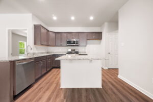 Modern kitchen interior with dark wood cabinets, stainless steel appliances, and an island, featuring hardwood floors and neutral walls.