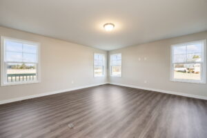 Empty room with light brown wood floors, beige walls, four windows, and a ceiling light fixture.
