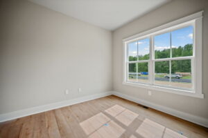 An empty room with light-colored walls, a large window showing a view of the outdoors, and light hardwood flooring.