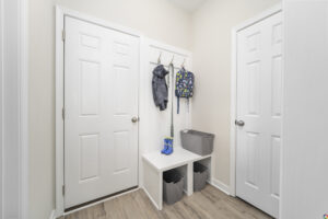 A small, tidy entryway with two white doors, a bench with storage cubes underneath, and hooks holding a jacket and a backpack.