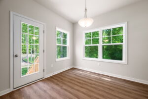 Empty room with hardwood floors, white walls, three windows, a glass door leading to a deck, and a hanging light fixture.