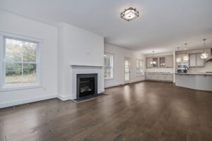 Spacious open-concept living area with hardwood floors, a fireplace, modern lighting fixtures, and a large kitchen featuring white cabinets, an island, and multiple pendant lights.