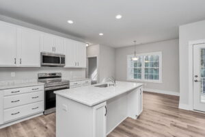 Modern kitchen interior with white cabinetry, stainless steel appliances, marble countertops, and hardwood flooring.