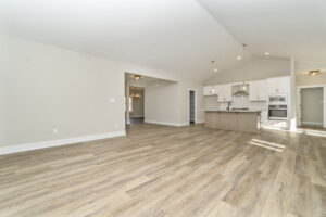 Empty modern kitchen and living room with open floor plan, featuring hardwood floors, white walls, and built-in appliances.