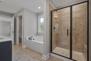 Modern bathroom featuring a glass-enclosed shower, a separate bathtub, a toilet in a small room, and a sink counter. The room has tiled floors and a window allowing natural light.
