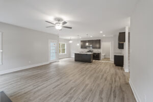 An open-concept kitchen and living room with wood floors, dark cabinetry, recessed lighting, ceiling fan, and French doors leading to an outdoor area.