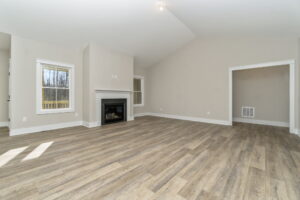 Empty living room with beige walls, vinyl flooring, a fireplace, and sunlight casting shadows on the floor.