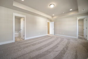Empty residential room with striped carpet, white walls, and multiple doors including one open to a bathroom.
