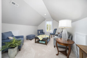 Bright, modern attic living room with sloped ceilings, featuring a blue sofa, matching chairs, a wooden coffee table, and ample natural light from a window.